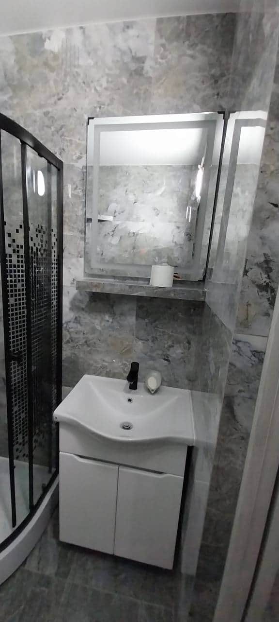 Zona de lavoar finalizată, cu oglindă iluminată, poliță placată și baterie neagră.